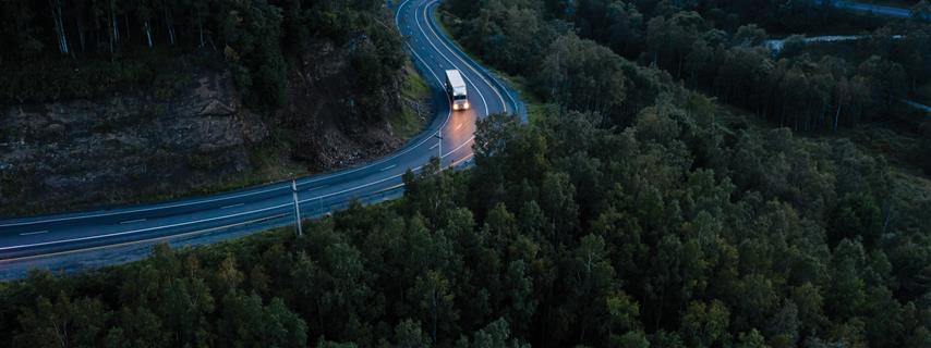 Truck drives along a winding road through a forest at night