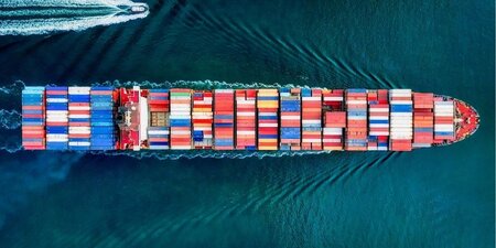 a large fully loaded container ship from above sailing on aqua water flanked by a smaller pilot boat