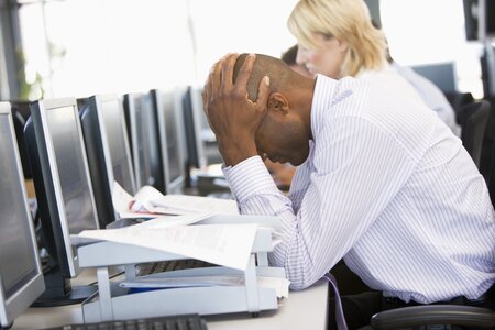 Stressed man in white shirt with head in hands on desk