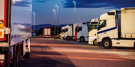 Lorries in a lorry park at dusk lit up by overhead lighting with an inky blue sky