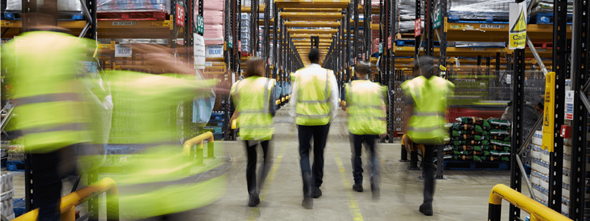Staff In Reflective Vests Walking In A Warehouse Back View Web